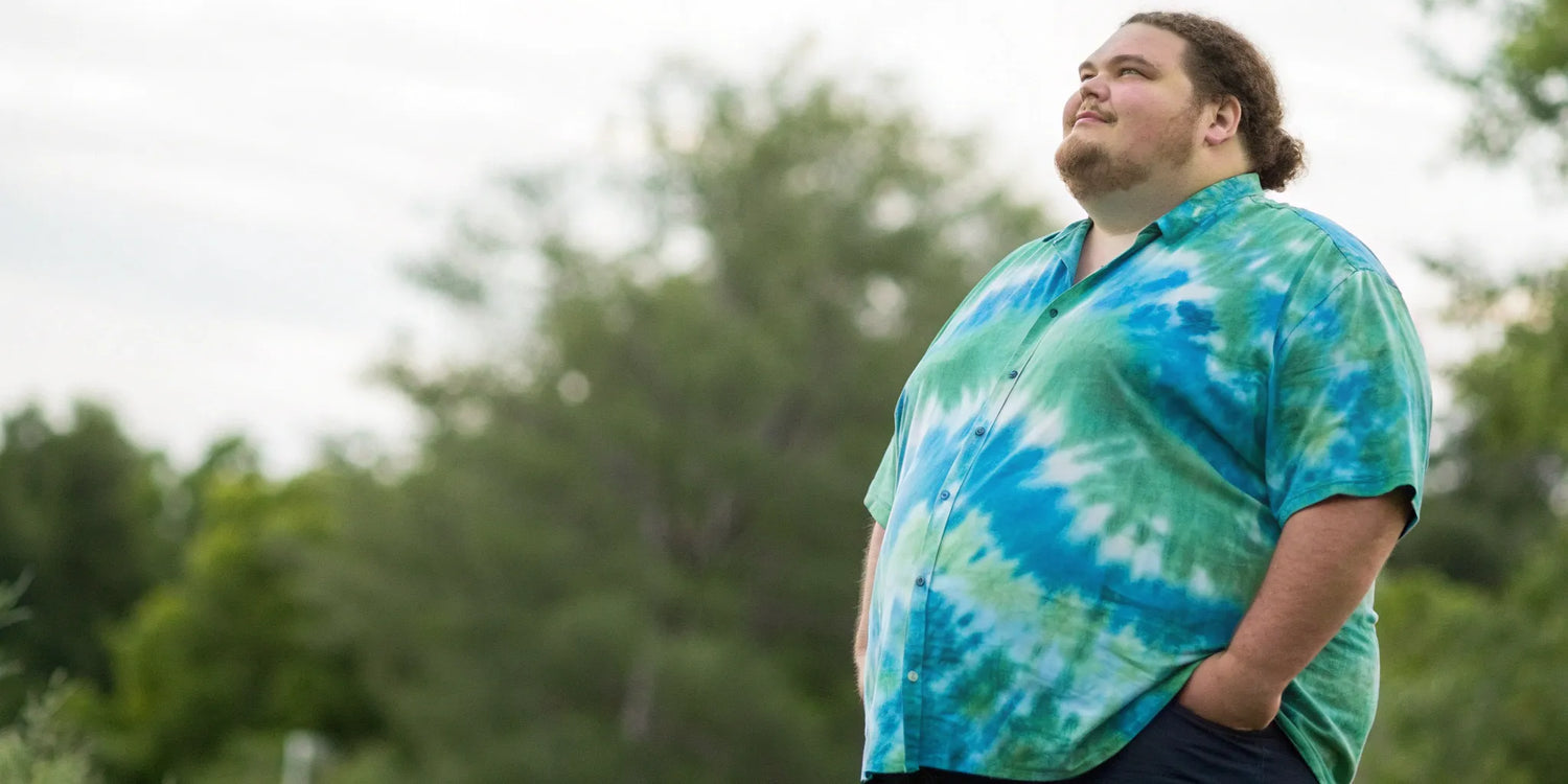 A big and tall man wearing a vibrant blue and green 6X tie dye shirt.