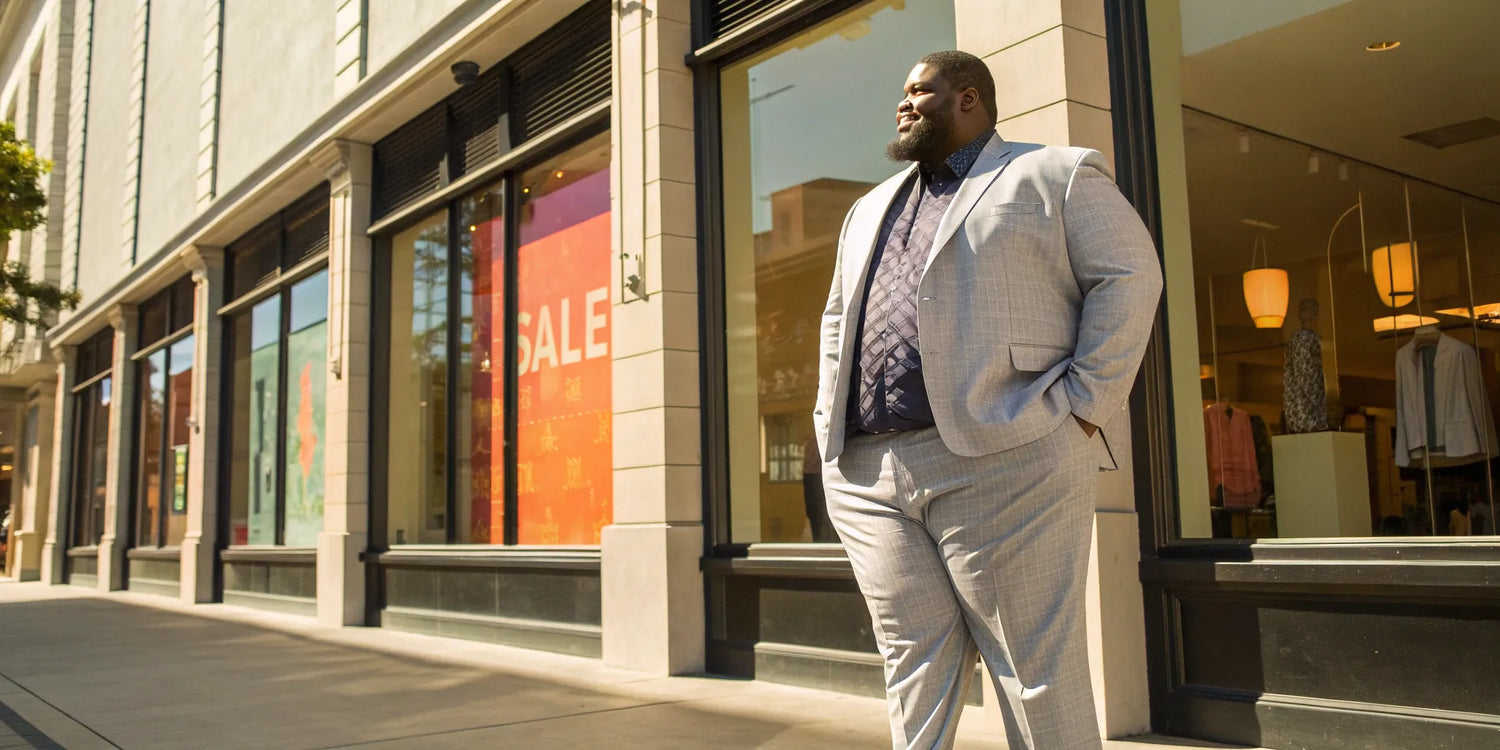 A stylish big and tall man standing outside a clothing outlet with sale signs.