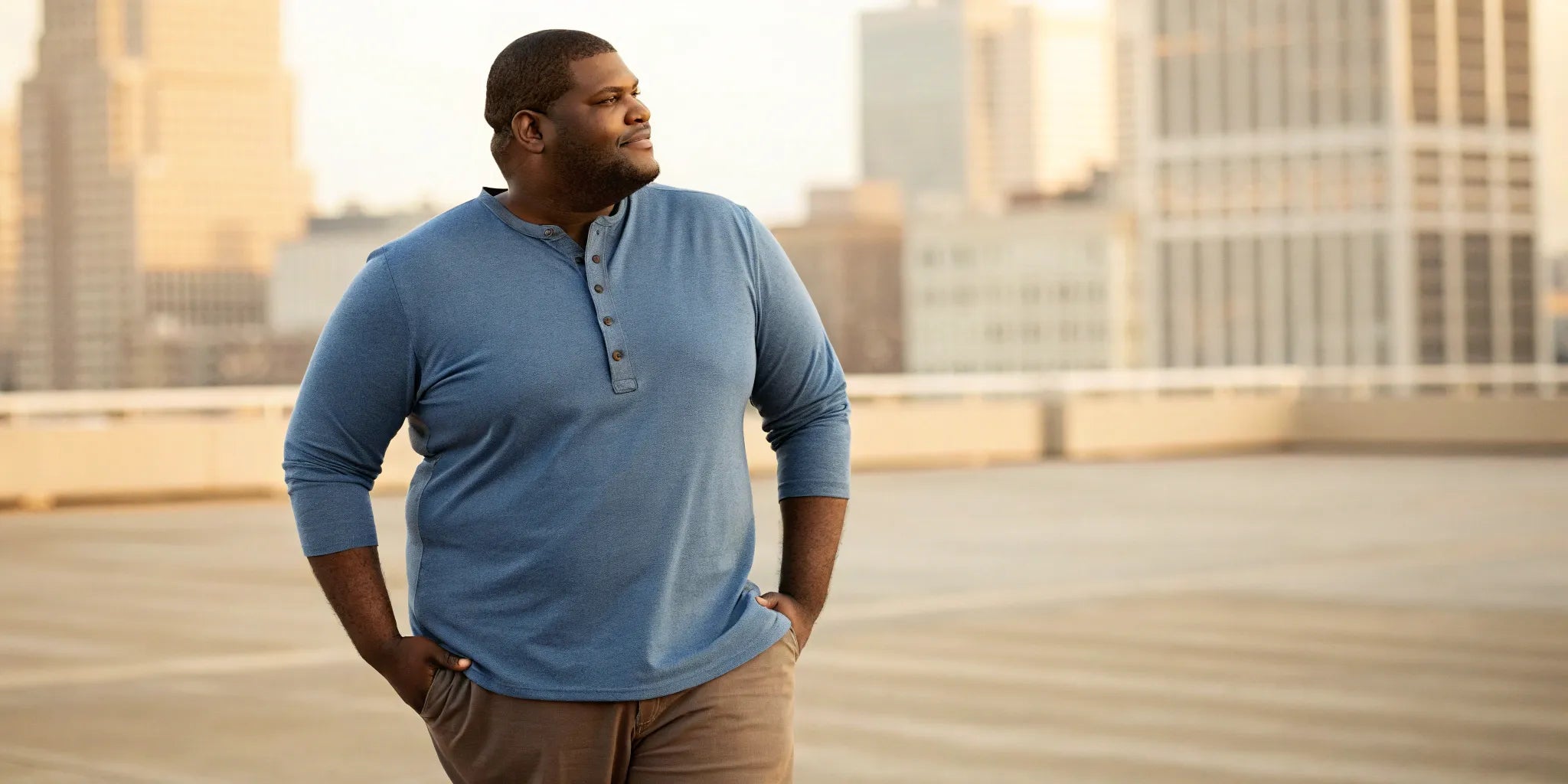 A big guy wearing a well-styled blue henley shirt and khaki pants.