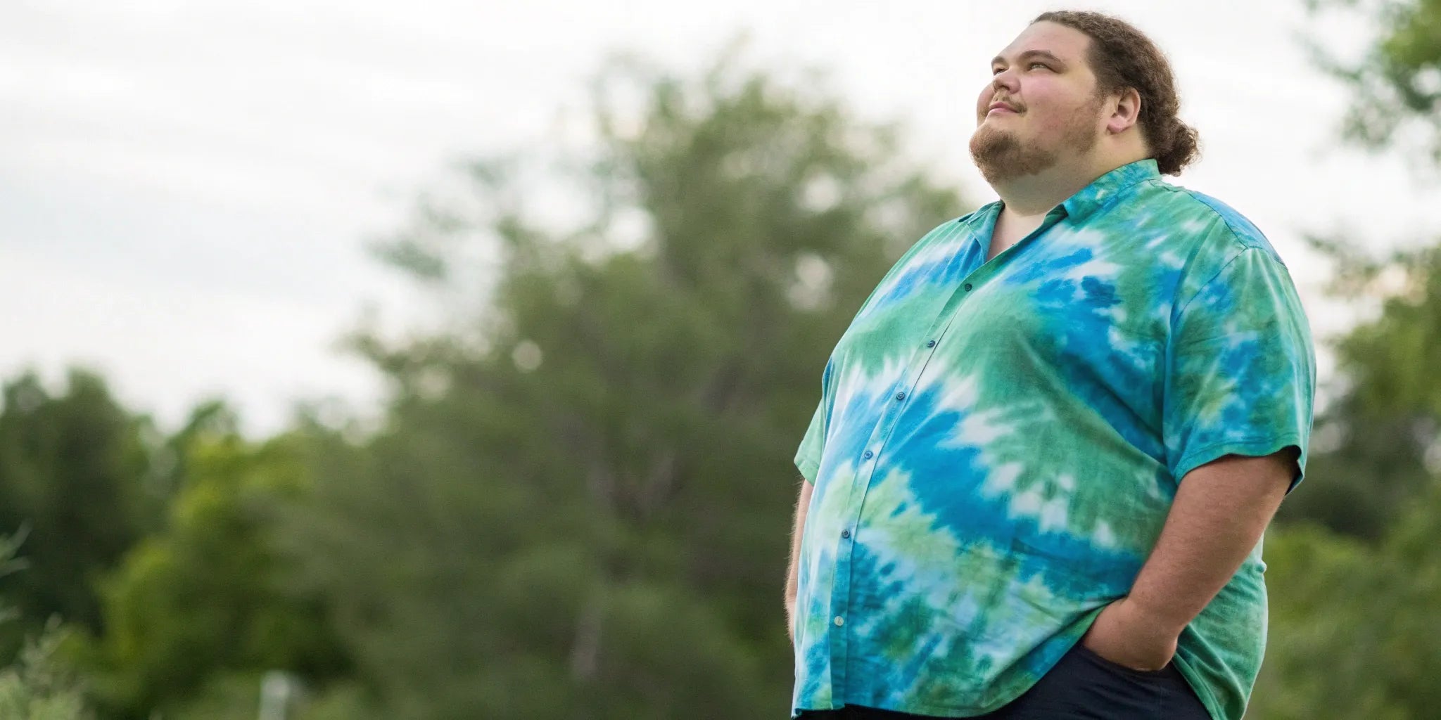 A big and tall man wearing a vibrant blue and green 6X tie dye shirt.